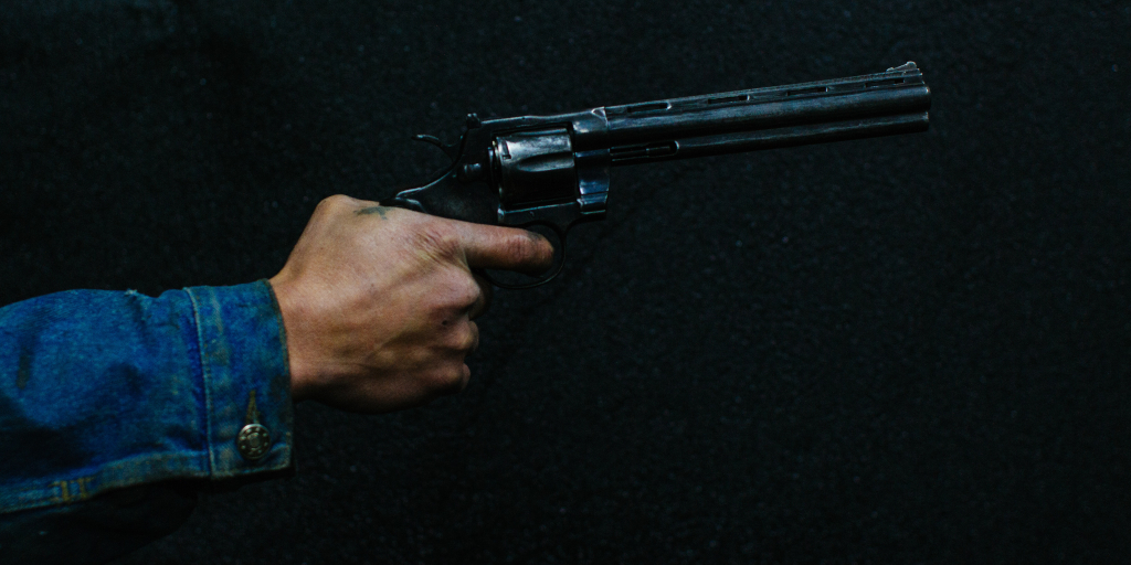 Static is Movement_Photo by Alejo Reinoso on Unsplash. Hand holding a gun. Person is wearing a blue denim jacket. Only the arm and hand are showing.