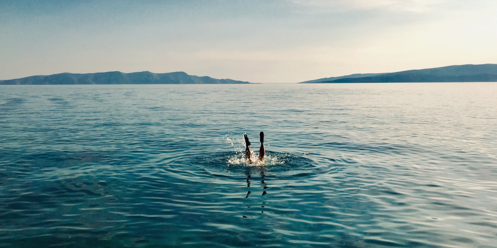 Blue Glass. Photo by Amy Lister on Unsplash. Shows a person's feet disappearing into the sea.